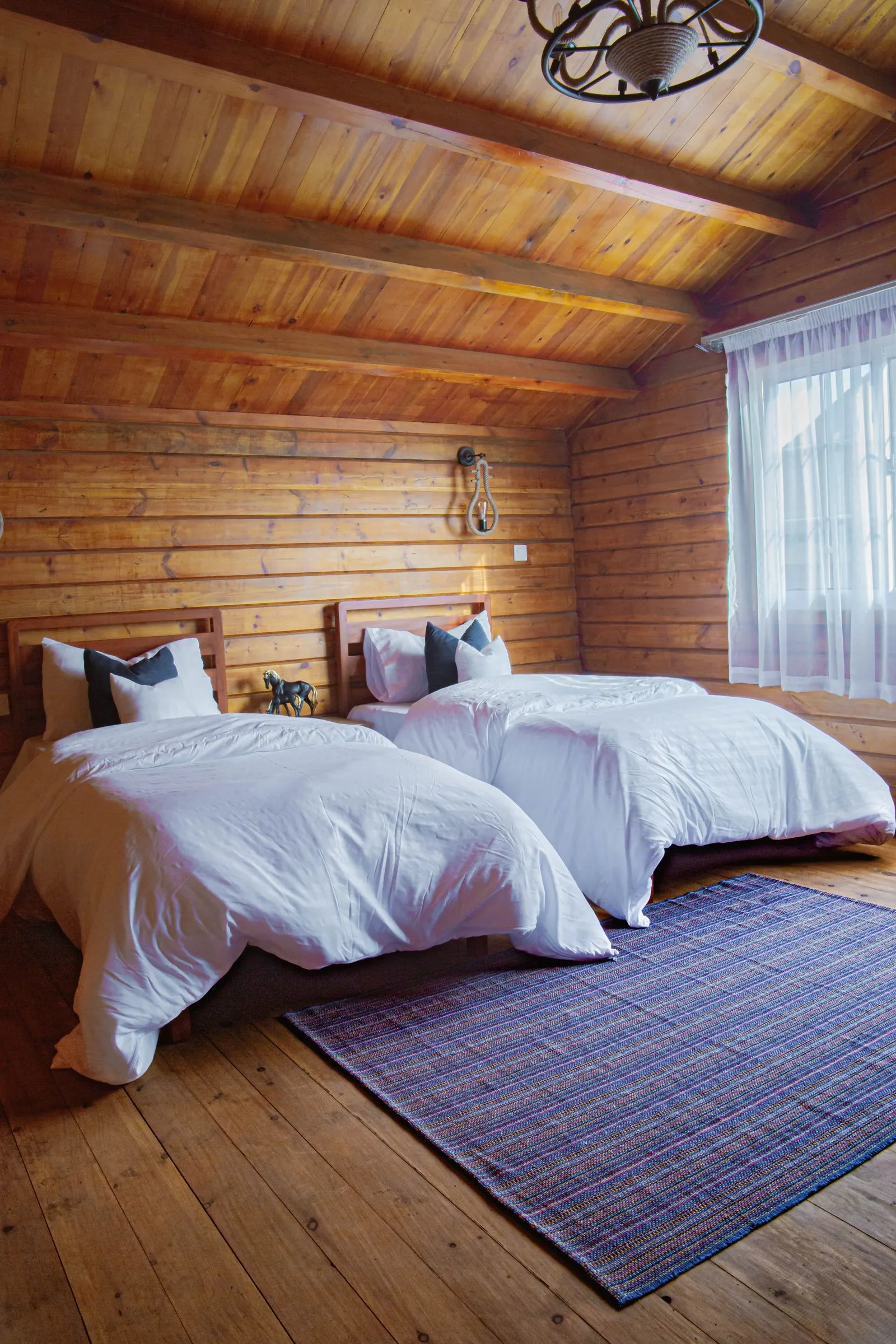 Habitación de casa rural con paredes de madera y camas con edredón blanco